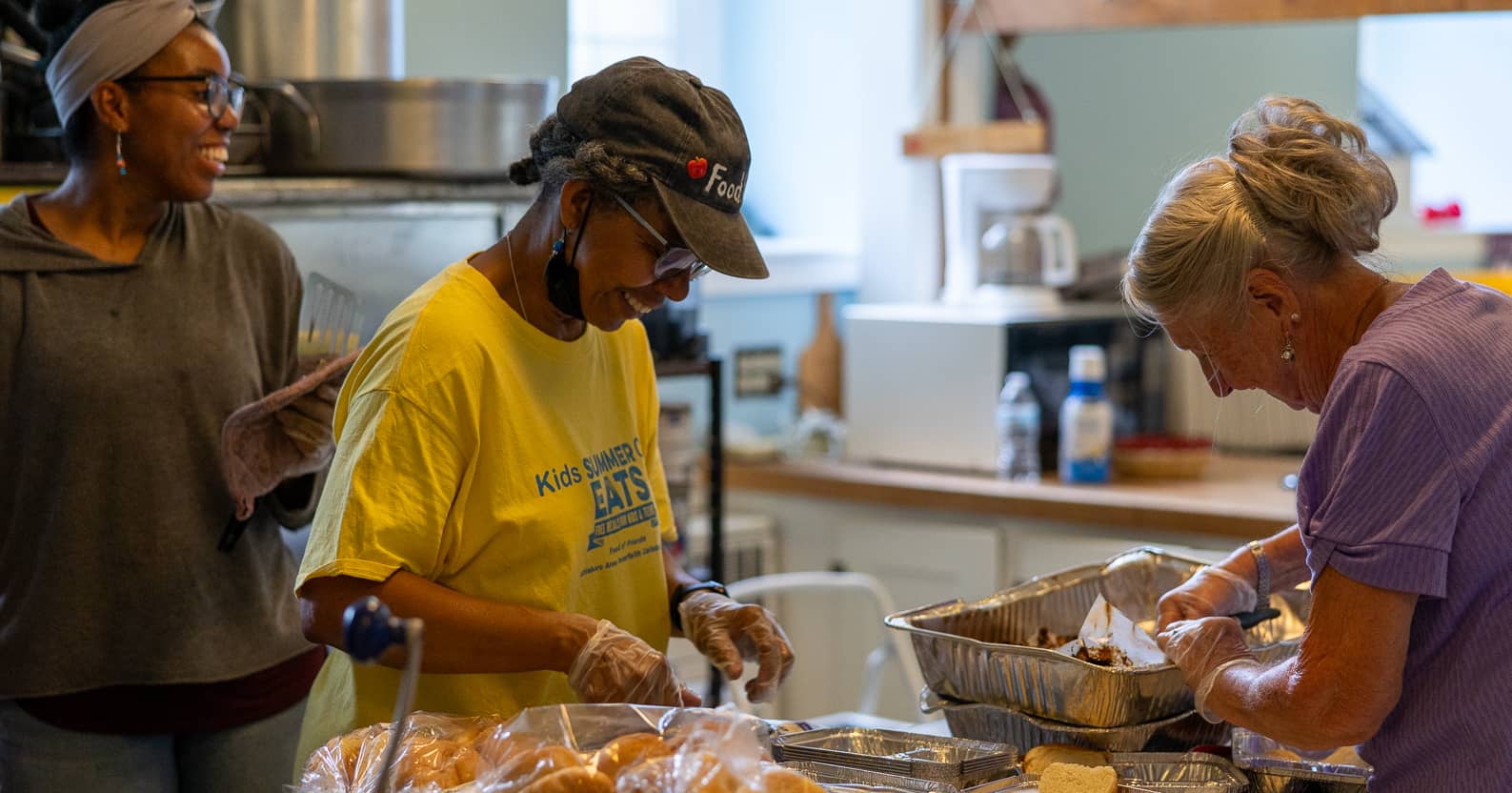Three people prepare meails in an industrial kitchen